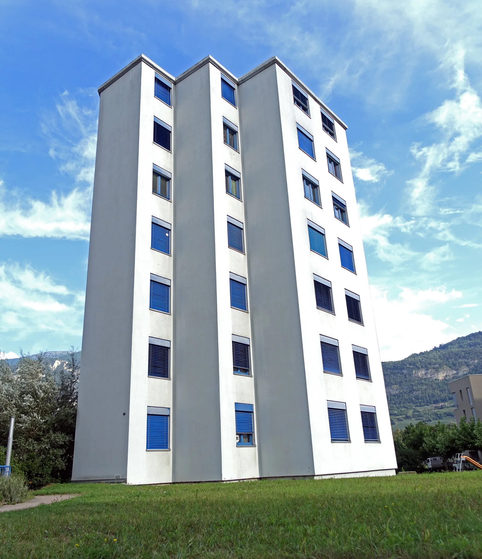 Immeuble d’habitation blanc à Sion, avec les montagnes en arrière-plan.
