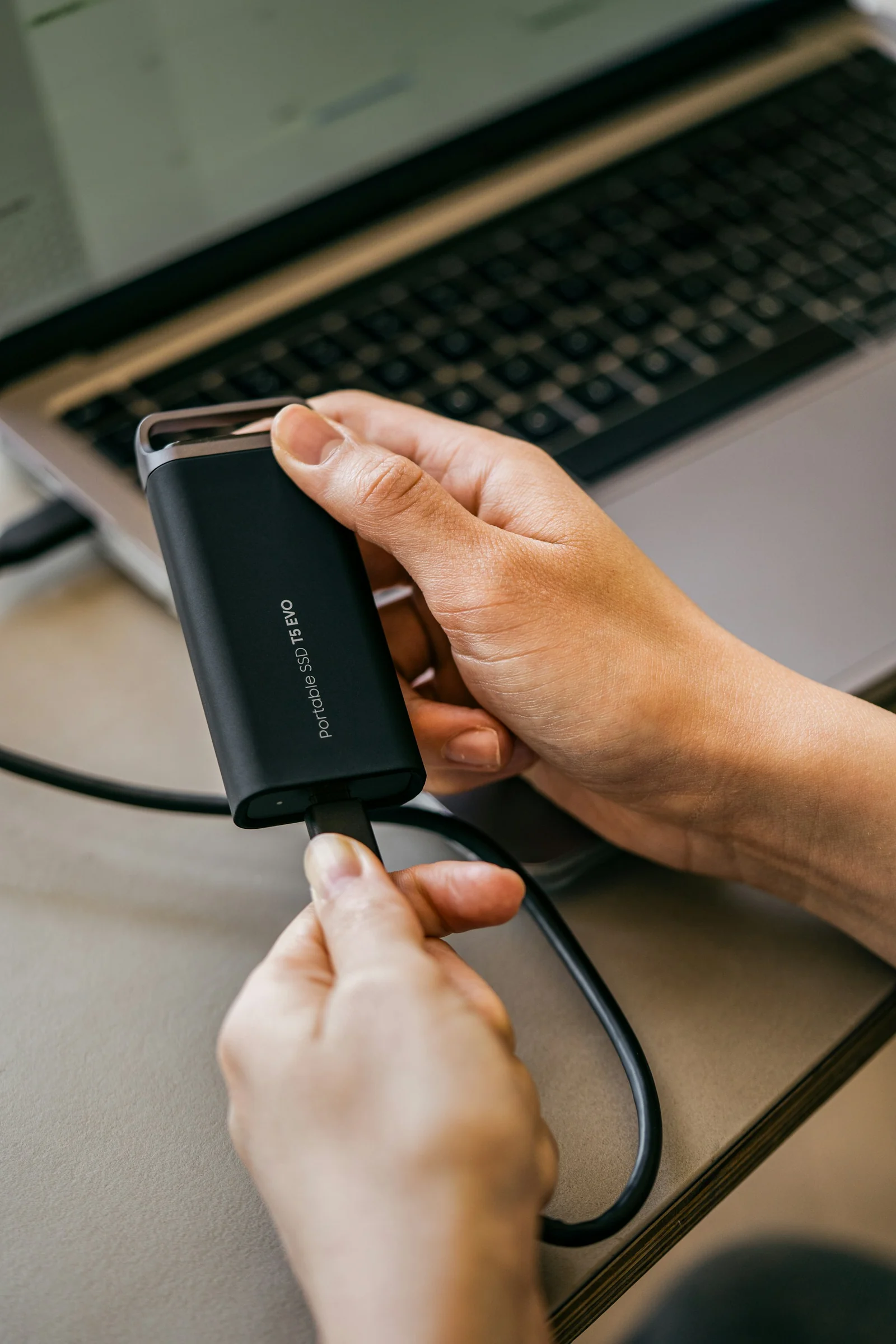 SSD externe tenu devant un ordinateur portable