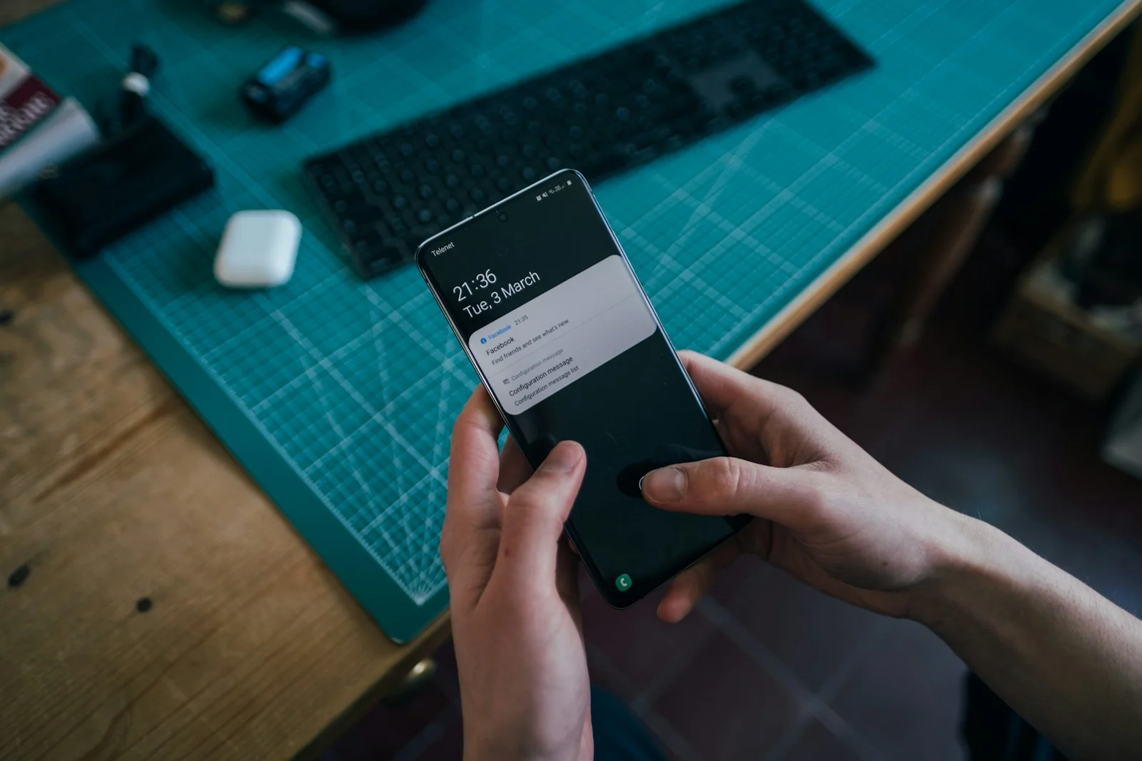 Mains tenant un smartphone à côté d’un ordinateur.