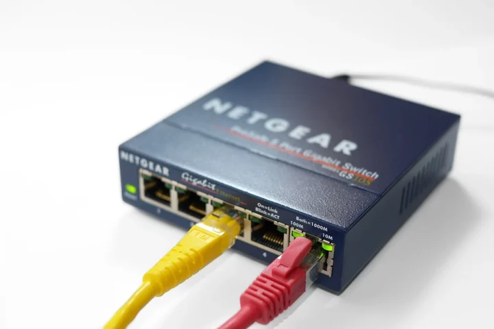 Commutateur Ethernet Netgear relié à deux câbles réseau. Modèle illustratif Gigabit, sans promesse de débit 2,5 Gb/s.