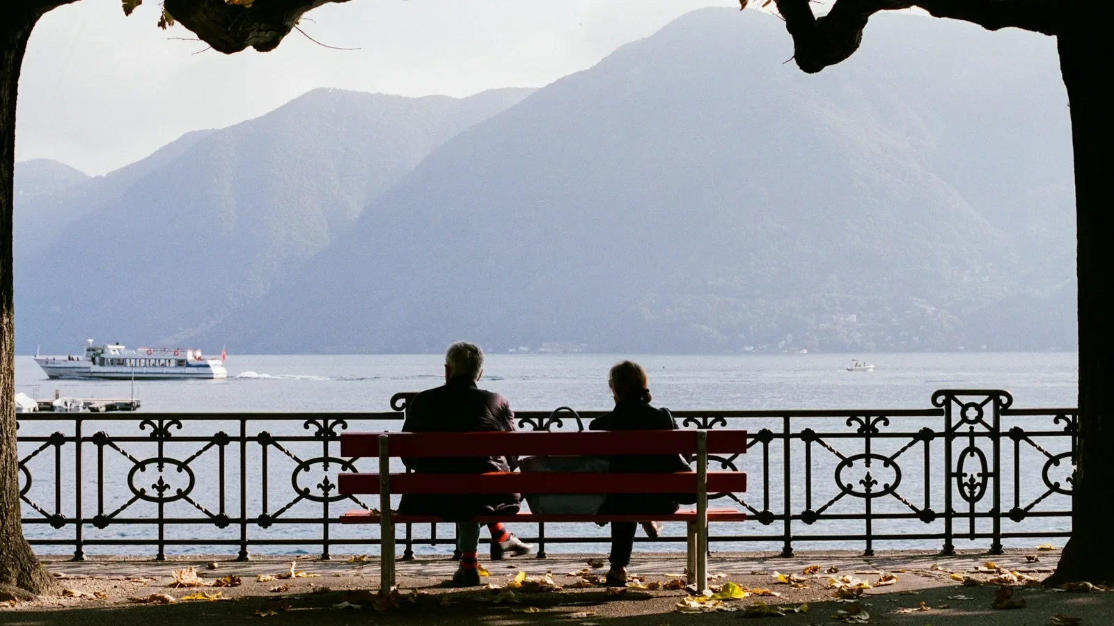 Deux personnes sur un banc rouge devant le lac de Lugano.