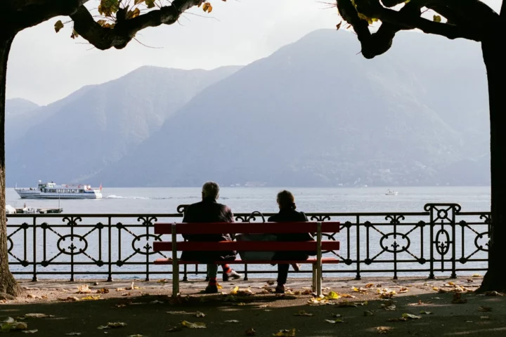 Deux personnes sur un banc rouge devant le lac de Lugano.