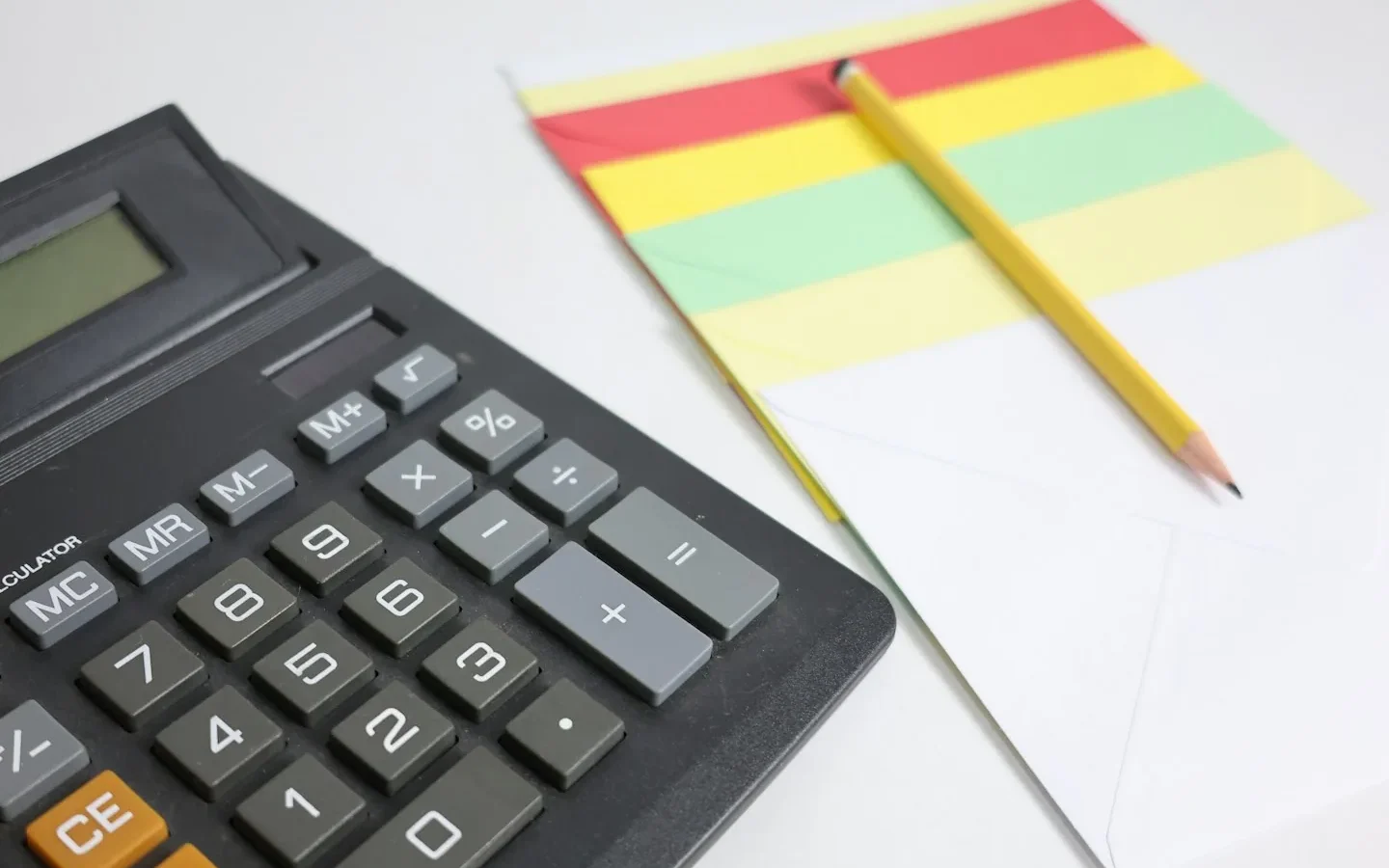 Calculatrice, crayon et bloc de notes sur une surface blanche.