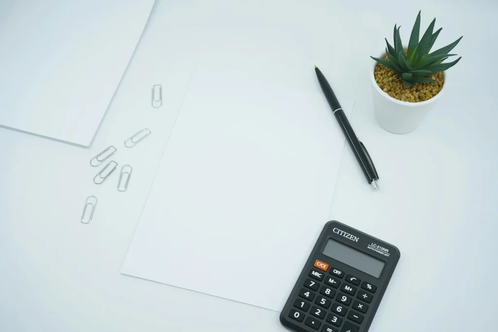 Calculatrice et stylo à côté d’une feuille blanche.