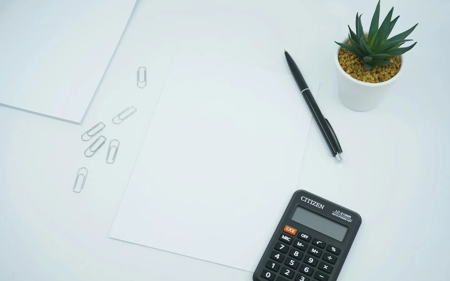 Calculatrice et stylo à côté d’une feuille blanche.