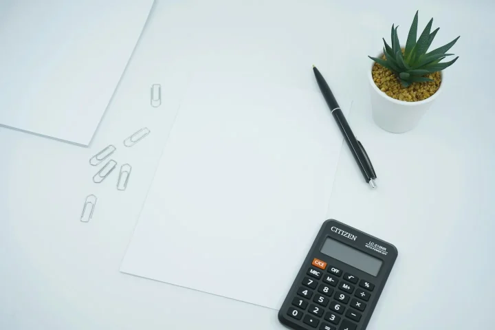 Calculatrice et stylo à côté d’une feuille blanche.