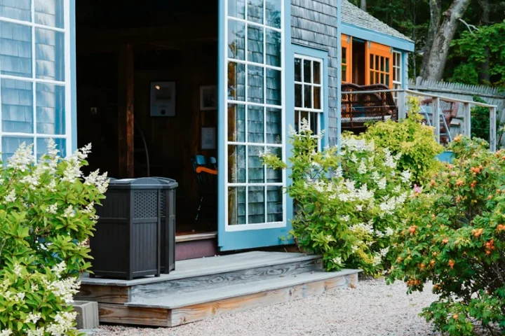 Portes vitrées ouvertes sur une terrasse entourée de plantes.