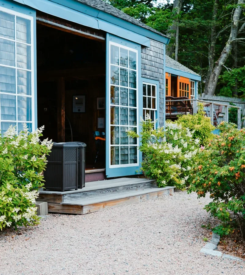 Portes vitrées ouvertes sur une terrasse entourée de plantes.