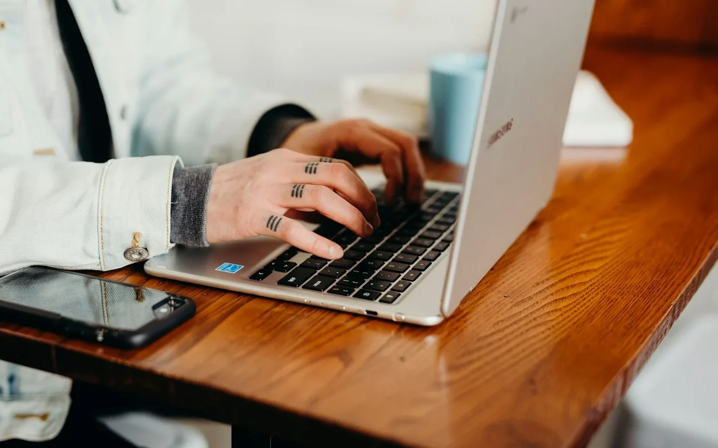 Mains sur le clavier d’un ordinateur portable, avec un téléphone à côté.