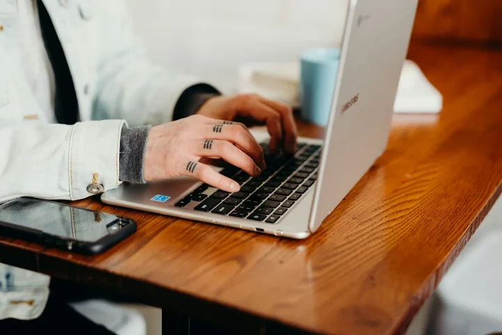 Mains sur le clavier d’un ordinateur portable, avec un téléphone à côté.